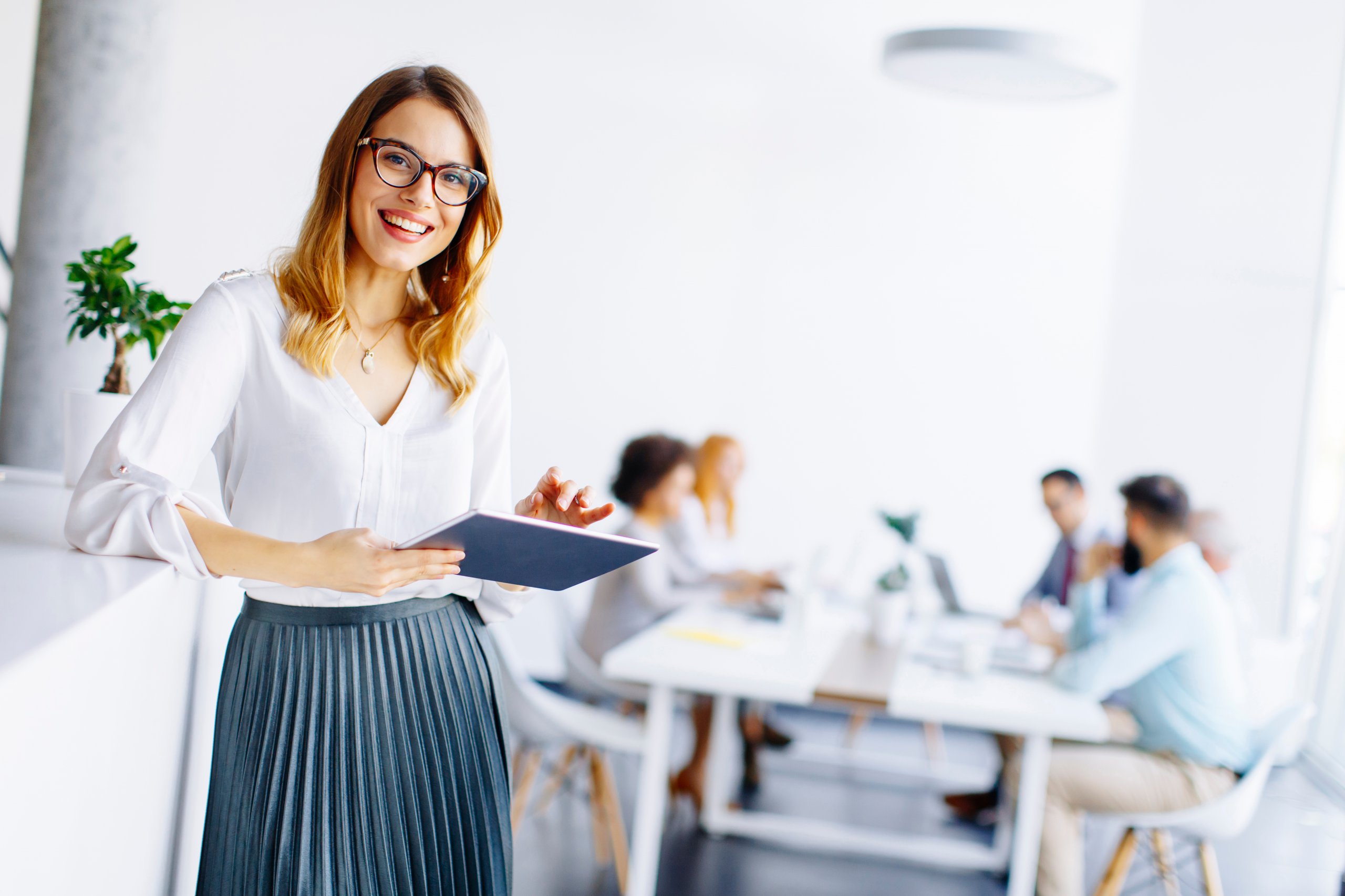 Young attractive female manager working on digital tablet while standing in modern office