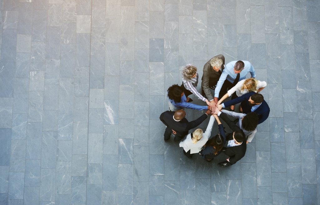 From above black and white office working people having teambuilding in hall standing with hands stacked.