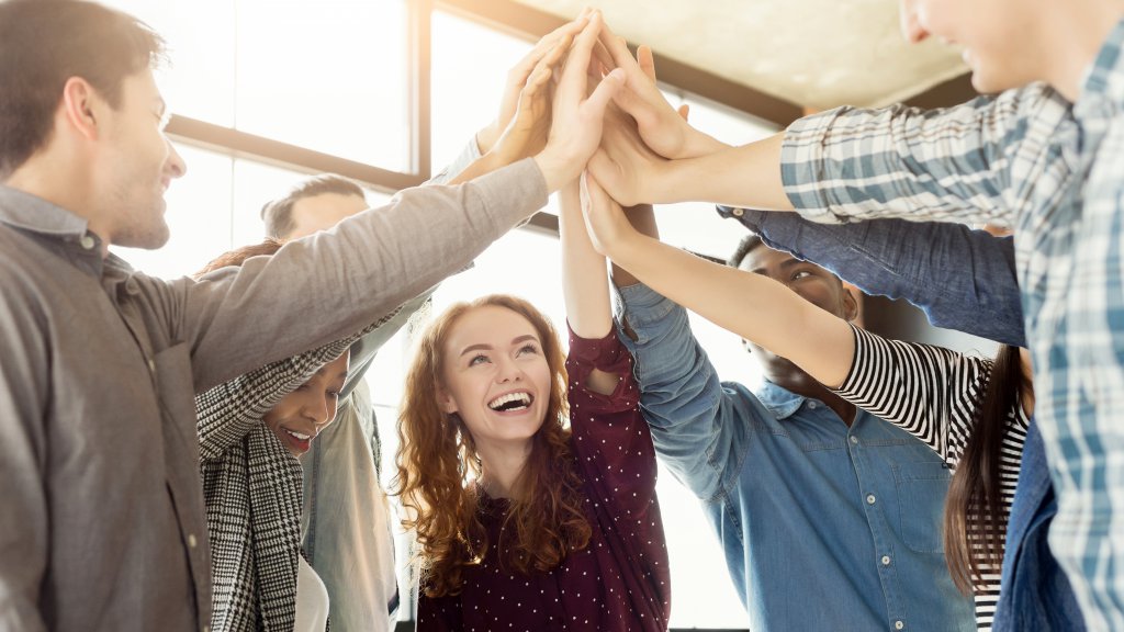 Teambuilding and unity background. Happy coworkers giving group high five in loft office, celebrating achievement