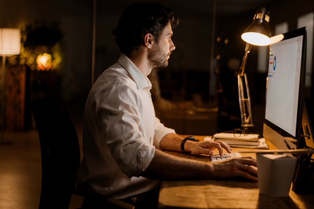 White bearded man working with computer in evening at office indoors