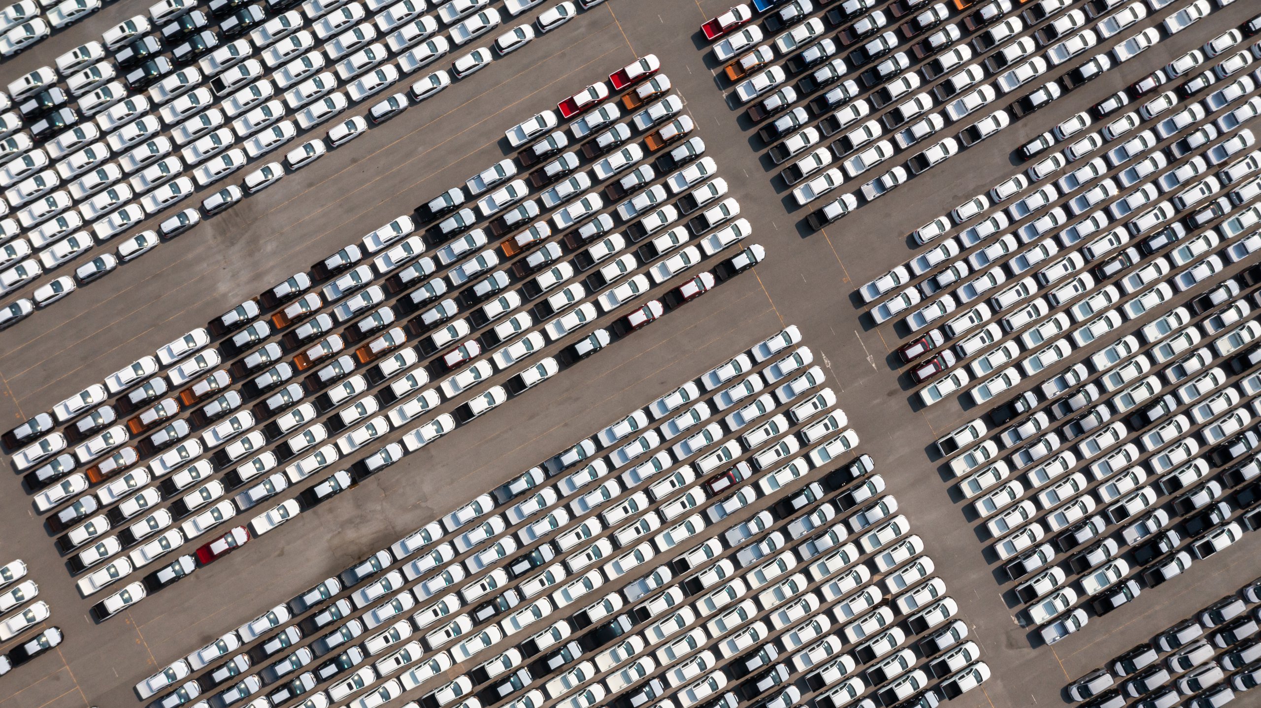 Aerial top view parked new cars at the automotive plant, new car lined up in the port for import and export business logistic to dealership for sale, Automaker distribution center with new vehicles.