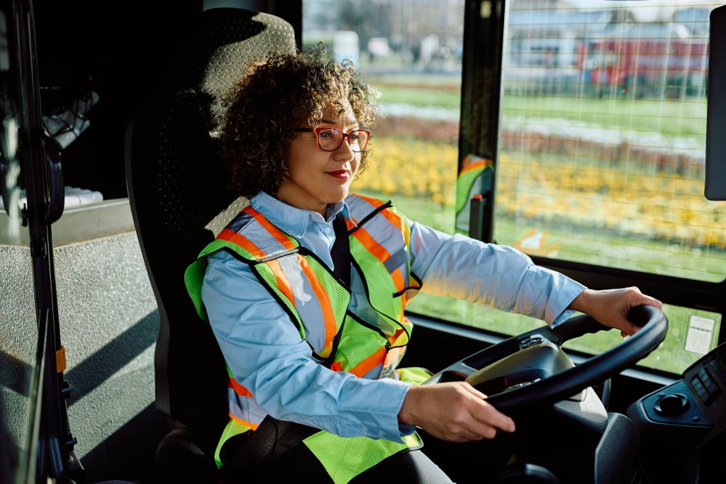 Happy female bus driver driving on city streets.