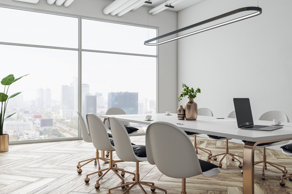 Perspective view on stylish white meeting table with golden legs and wheel chairs around on wooden floor and white wall background in sunlit conference area with city view backdrop.