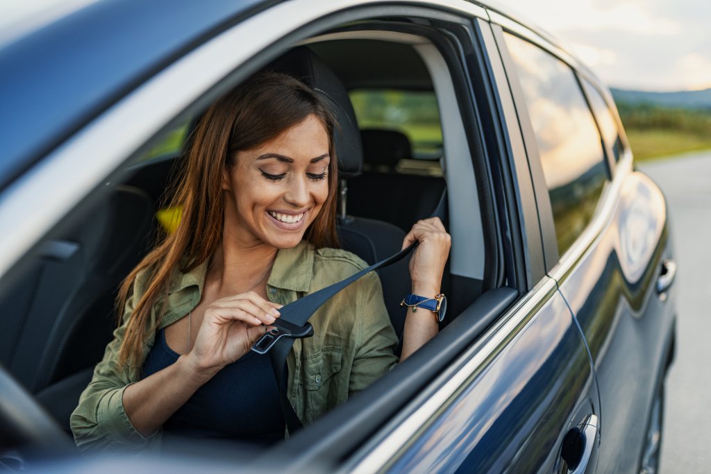 Young attractive woman sitting on car seat and fastening seat belt, car safety concept.