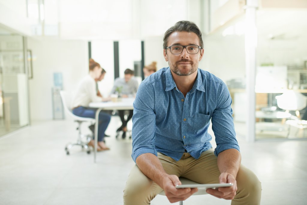 Portrait of a mature man using a digital tablet at work with his team working in the background