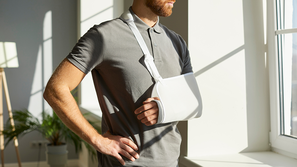 homme ayant le bras cassé, avec un plâtre, regardant par la fenêtre