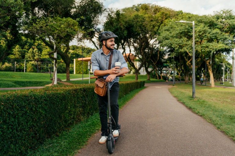 Homme sur sa trottinette électrique en train de regarder au loin avec son café à emporter.