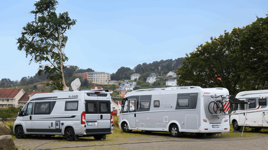 Un van aménagé et deux camping car stationnés sur un point de vue avec vue sur un village en arrière plan.
